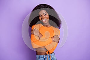 Photo of shiny sweet dark skin lady wear orange shirt embracing herself isolated violet color background photo