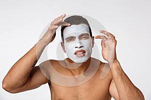 Photo of shirtless african american man smiling and applying face cream isolated over white background