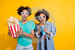 Photo of shocked afro american people couple wear 3d glasses movie pop corn fly drink isolated on yellow color