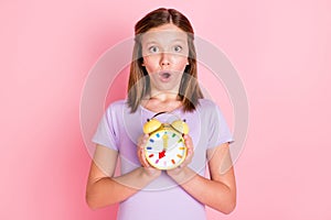 Photo of shocked amazed little teenage girl hold hands alarm clock time isolated on pink color background