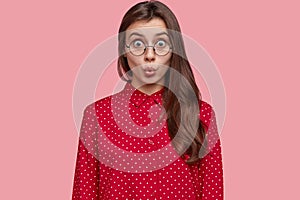Photo of shocked woman in stupor, keeps lips round, has distrubing situation, dressed in fashionable polka dot blouse photo