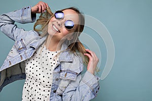 Photo shot of attractive happy smiling young blonde woman wearing summer casual clothes and stylish sunglasses isolated