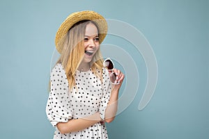 Photo shot of attractive happy smiling young blonde woman wearing summer casual clothes and stylish sunglasses isolated