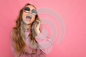 Photo shot of beautiful overjoyed young dark blonde curly woman isolated over pink background wall wearing casual pink