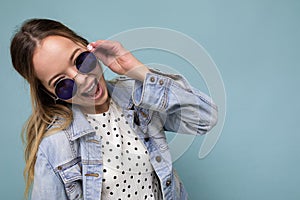 Photo shot of beautiful positive surprised young blonde woman wearing summer casual clothes and stylish sunglasses