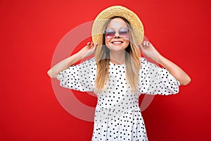 Photo shot of beautiful positive young blonde woman wearing summer casual clothes and stylish sunglasses isolated over