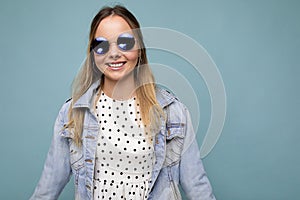 Photo shot of beautiful positive young blonde woman wearing summer casual clothes and stylish sunglasses isolated over