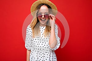 Photo shot of beautiful positive young blonde woman wearing summer casual clothes and stylish sunglasses isolated over