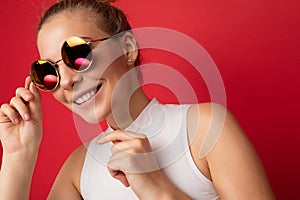 Photo shot of beautiful smiling positive young blonde woman wearing casual clothes and stylish sunglasses  over