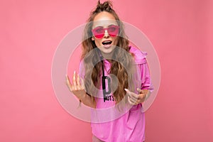 Photo shot of beautiful surprised young dark blonde woman wearing casual clothes and stylish sunglasses isolated over