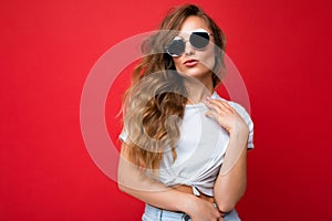 Photo shot of beautiful young blonde woman wearing casual clothes and stylish sunglasses isolated over colorful