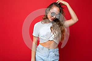 Photo shot of beautiful young dark blonde woman wearing casual clothes and stylish sunglasses isolated over colorful