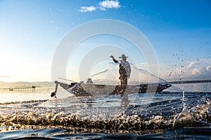 Photo shot of water spatter from fisherman while throwing fishing net on the lake. Silhouette of fisherman with fishing net in mo