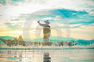 Photo shot of water spatter from fisherman while throwing fishing net on the lake. Silhouette of fisherman with fishing net in