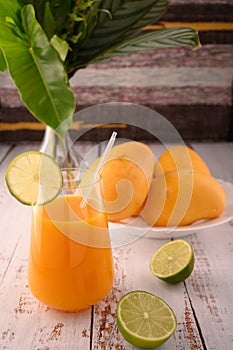 Mango martini and plate of mango and lime. Vase with tropical leaves on left