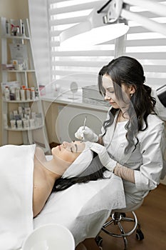 The photo shows a professional cosmetologist performing deep cleansing of a young woman& x27;s face, providing her with