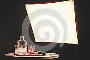 A photo-shutting setup, with light, and candle, a bottle, a watch, a wallet, and glasses on a table