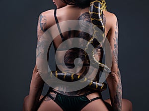 Photo of the sitting woman with crawling yellow anaconda on back