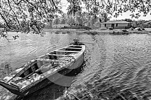 Small boat moored by the river. A house and trees.