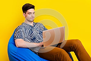 Photo of smart clever man dressed print shirt brown trousers typing email on laptop sit on bean bag isolated on yellow