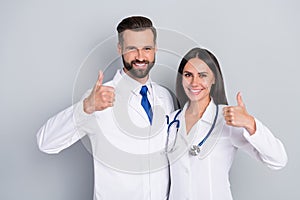 Photo of smart happy two docs dressed white coats embracing showing thumbs up  grey color background