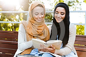 Photo of smart islamic girls wearing headscarfs sitting in green park