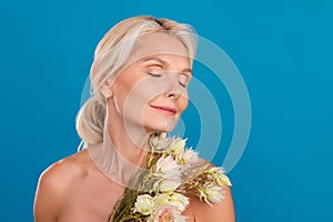 Photo of smiling adorable elderly lady naked shoulders enjoying bunch aroma closed eyes empty space isolated blue color