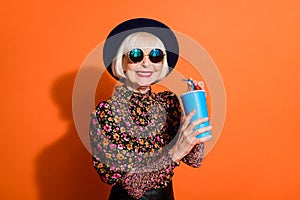 Photo of smiling cheerful good mood happy grandmother hold fizzy drink cola soda isolated on orange color background