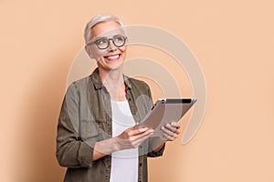 Photo of smiling cheerful mature businesswoman in casual outfit look empty space tablet app notion isolated on beige