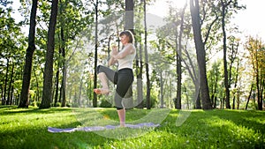 Photo of smiling happy woman 40 years old doing yoga exercises on fitness mat at forest. Harmony of human in nature