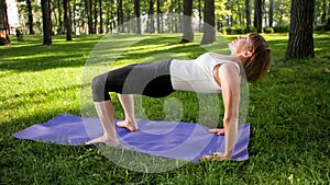 Photo of smiling happy woman 40 years old doing yoga exercises on fitness mat at forest. Harmony of human in nature