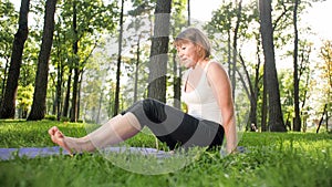 Photo of smiling happy woman 40 years old doing yoga exercises on fitness mat at forest. Harmony of human in nature