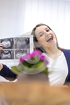 Photo of smiling pregnant woman holding ultrasound result.