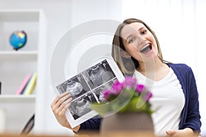 Photo of smiling pregnant woman holding ultrasound result.