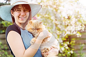 Photo of smiling woman in hat holding ginger cat in garden