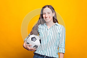 Photo of smiling young woman holding soccer ball over yellow background