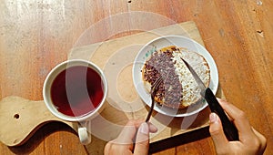 A photo of someone eating a mini martabak and drinking a cup of tea on a wooden table