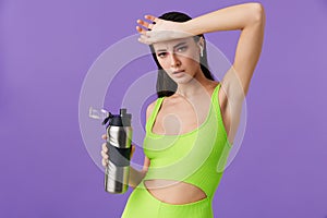 Photo of sporty confused woman using earpods and holding water bottle
