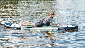 Photo of a Sporty Girl in a teen outfit resting on a SUP Board on the water after an active workout. Sports for teenagers.