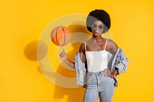 Photo of sporty young woman wear casual jeans clothes spinning finger basket ball isolated yellow color background