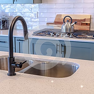 Photo Square frame Kitchen island double sink and black faucet against cooktop and tile backsplash