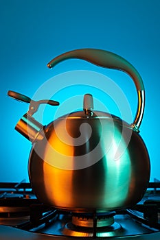 Photo of stainless steel kettle in neon light over blue background.