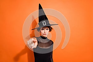 Photo of strict serious lady wear black witch dress cap pointing finger you empty space isolated orange color background