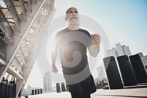 Photo of strong confident retired man black sportswear running fast sunrise outside urban city street