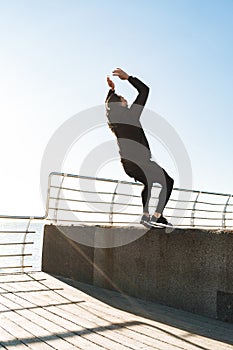 Photo of strong guy 20s doing acrobatics and jumping during morning workout by seaside