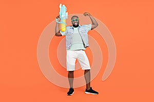 Photo of strong guy dressed jeans waistcoat dark glasses shooting water gun rising fist isolated orange color background