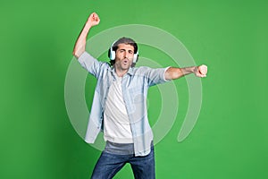 Photo of stubbled man raise arm posing dance wear headphones denim shirt jeans isolated green color background photo