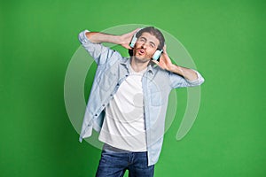 Photo of stubbled young man hands headset look camera wear earphones denim shirt jeans isolated green color background photo