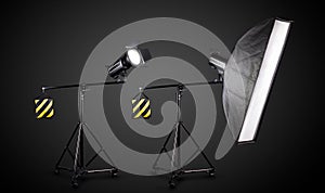 Photo studio lighting stands with flash and softbox isolated on the black.