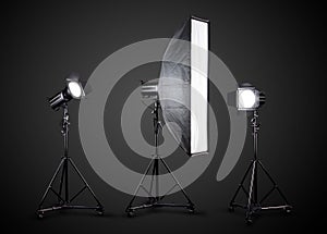 Photo studio lighting stands with flash and softbox isolated on the black.